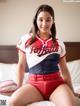 A woman in a baseball uniform sitting on a bed.