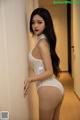 A woman in a white bodysuit leaning against a wall.