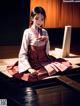 A woman in a kimono sitting on a wooden platform.