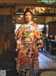 A woman in a kimono standing in front of a clock.