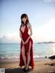 A woman in a red dress standing on a beach.