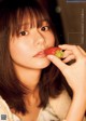 A woman holding a strawberry in front of her face.