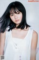 A woman with long black hair wearing a white tank top.